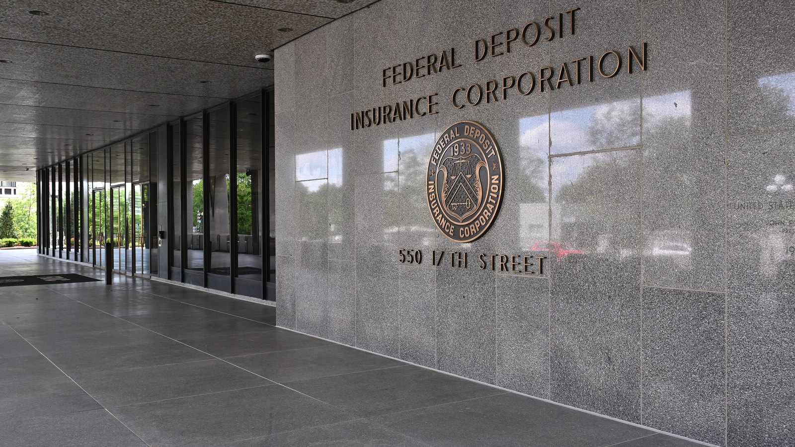The entrance to the Federal Deposit Insurance Corporation headquarters in Washington, D.C., its name and 1933 seal cut in bronze on a granite wall above the words 550 17th Street.