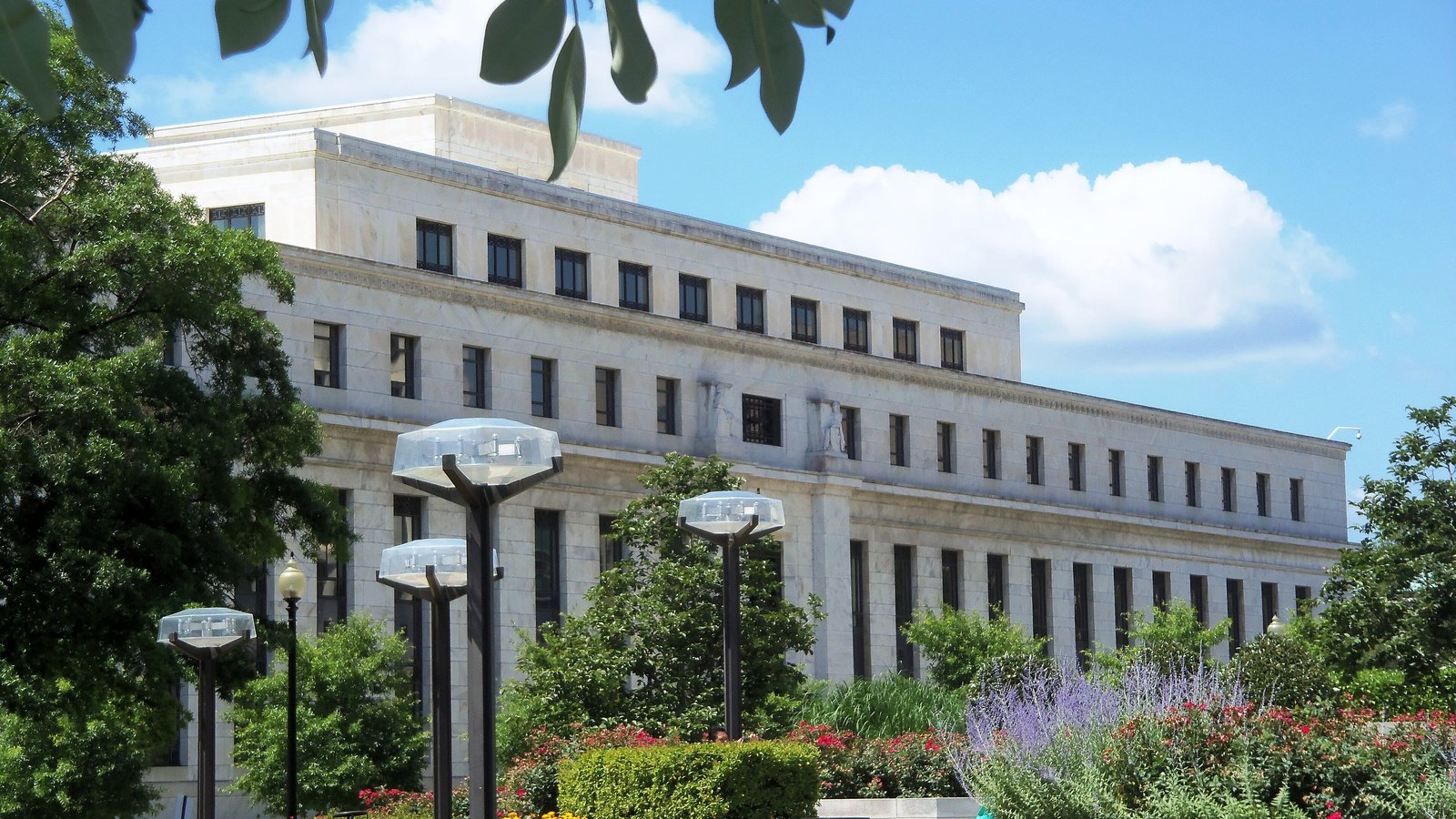 The white marble Marriner S. Eccles Federal Reserve Board Building seen across a landscaped garden in Washington.