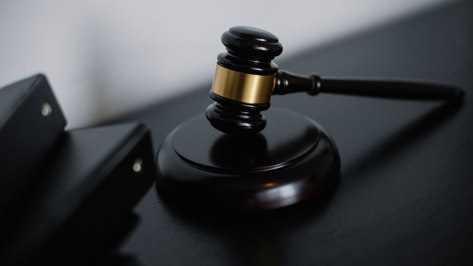 A wooden gavel resting on a dark desk beside a closed folder in low light. No text, person or place is visible. A generic illustration of an enforcement or sanctions action, not a photograph of anything in this story.
