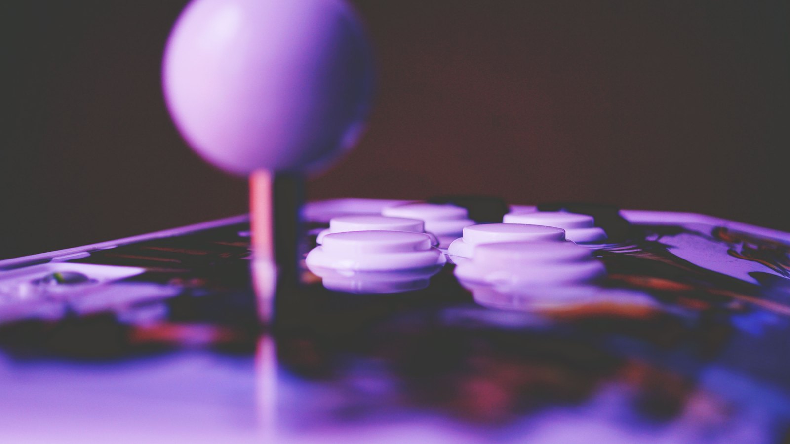 A purple-lit arcade joystick and white game buttons seen in close-up.