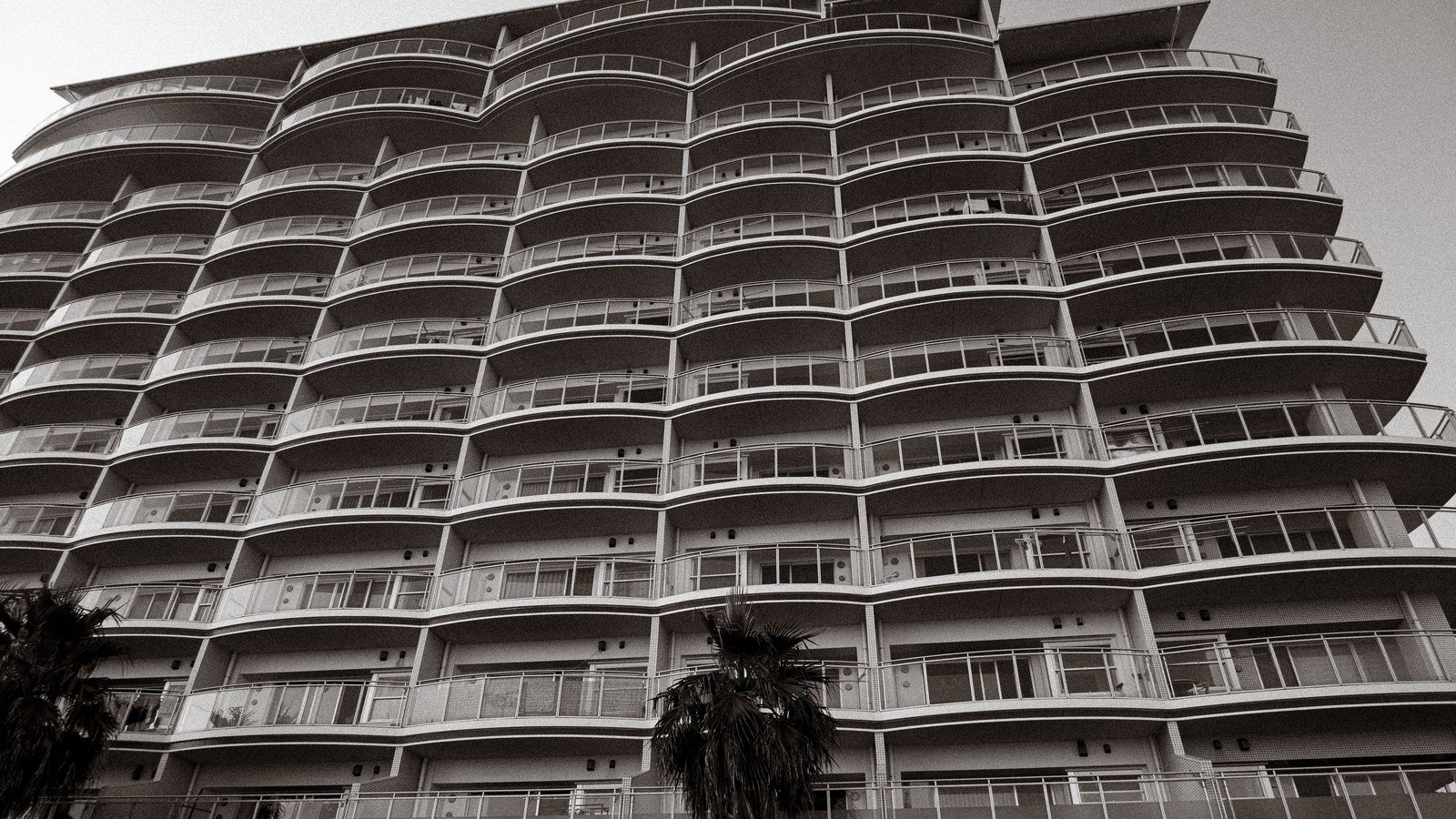 A high-rise residential tower with curved balconies behind palm trees, an illustration rather than a photograph of any building affected by the rule.