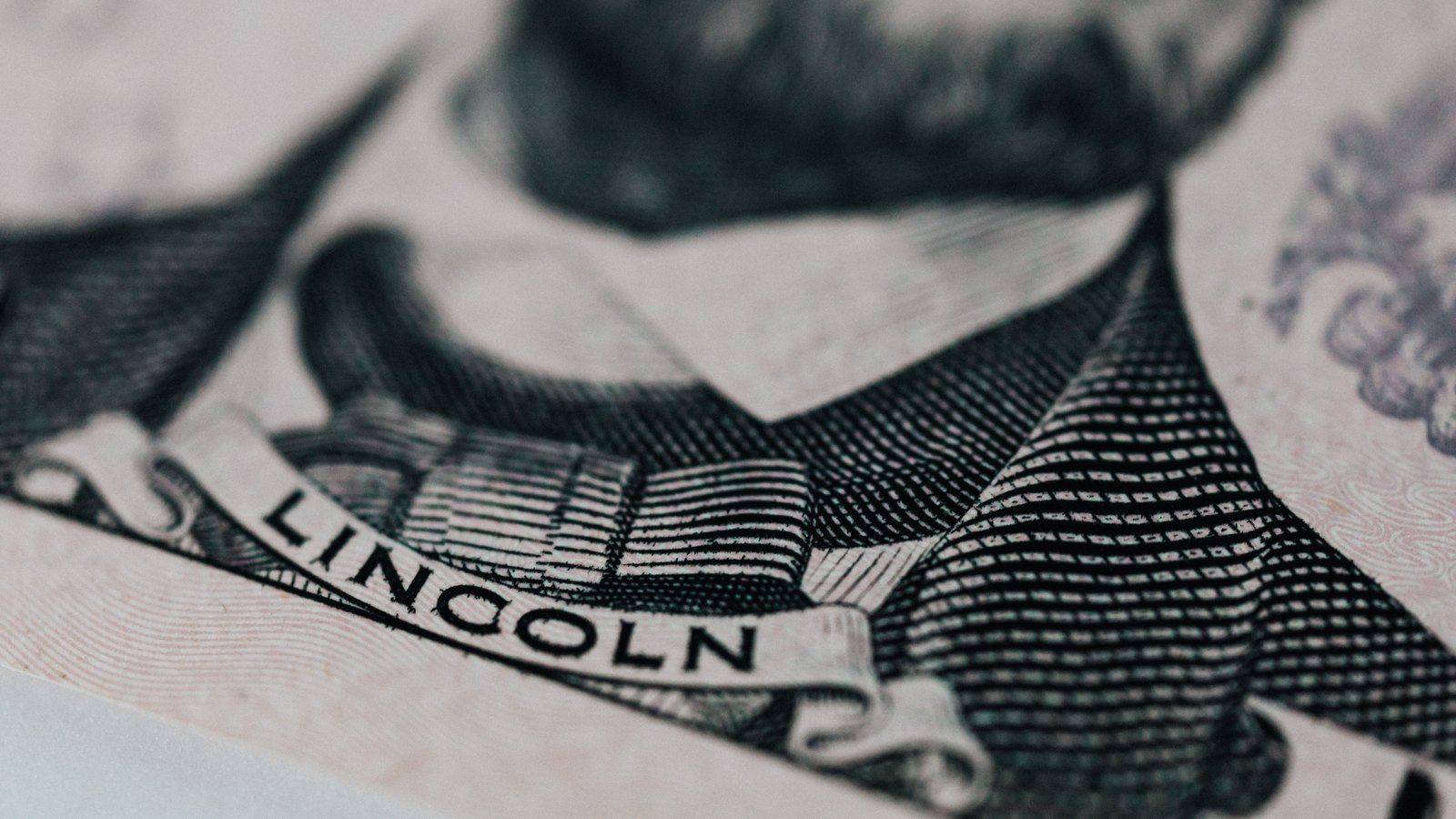 A very close photograph of the engraved detail on a United States five dollar bill, the fine line work of the Lincoln Memorial frieze with the name LINCOLN cut into the stone, shot at shallow depth of field.