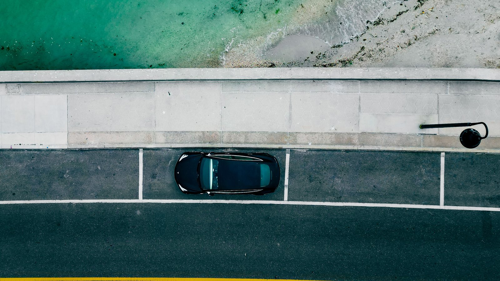 An overhead view of a parked car beside turquoise coastal water, not Fort Myers Beach.