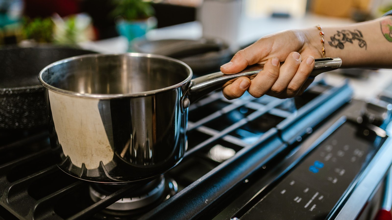 A hand lowers a stainless steel saucepan onto the grate of a black gas hob in a domestic kitchen, the pan empty and the burner not yet lit, with no brand name, place name or legible text in view.