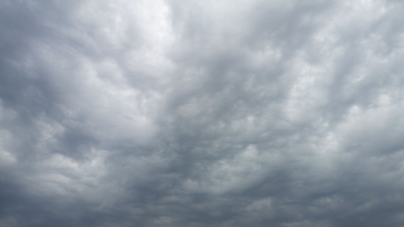 A flat overcast sky filling the frame, layers of grey cloud thinning to pale light near the top, with no horizon, buildings, people, signs or text in view.