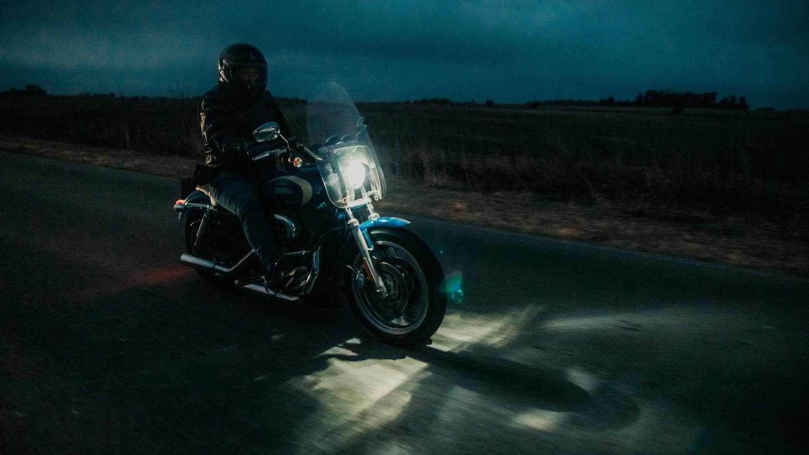 A helmeted motorcycle rider travels a dark road at night, not a photograph of this event.