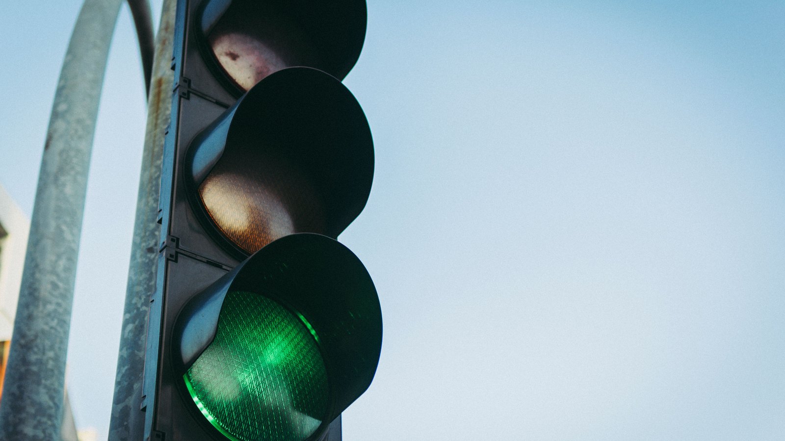 A traffic signal showing green, photographed from below against a pale blue sky.