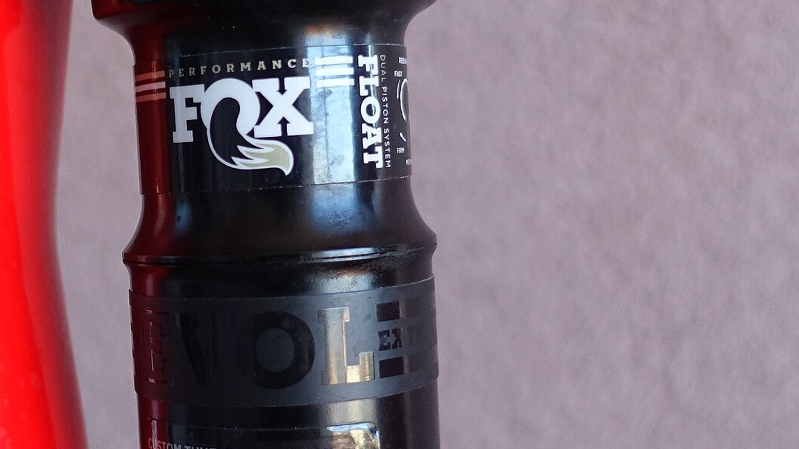 A close view of the black cylinder of a FOX Float rear bicycle shock beside a red frame.