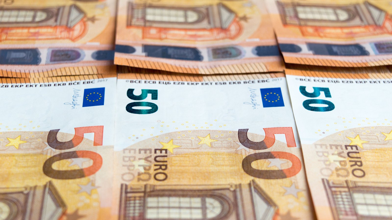 Overlapping 50 euro banknotes laid out in rows, with the European Central Bank acronyms and the European Union flag legible along the upper edge of each note.