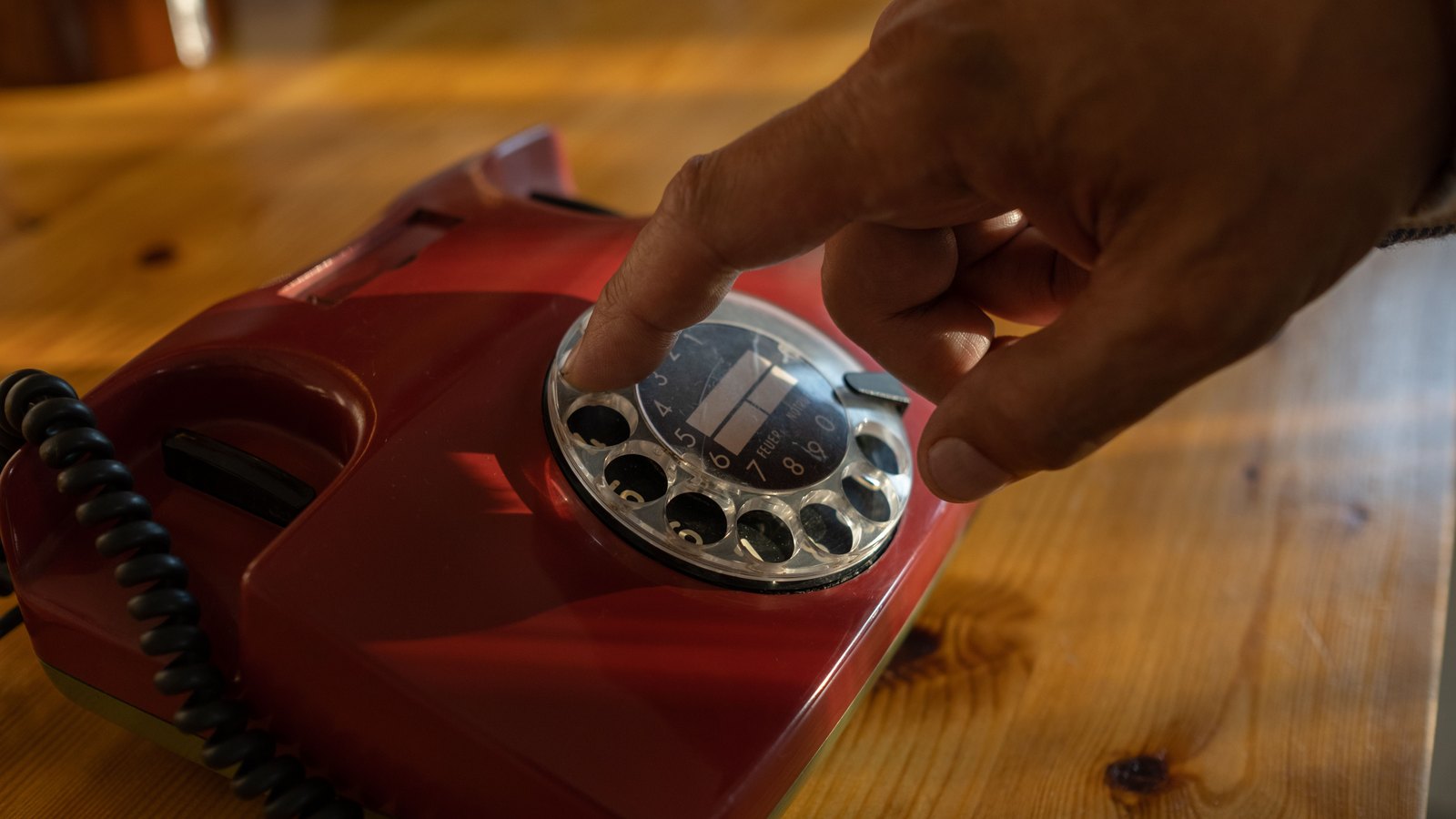 A hand dialing a red rotary telephone, a stock photo and not a photograph of this event.