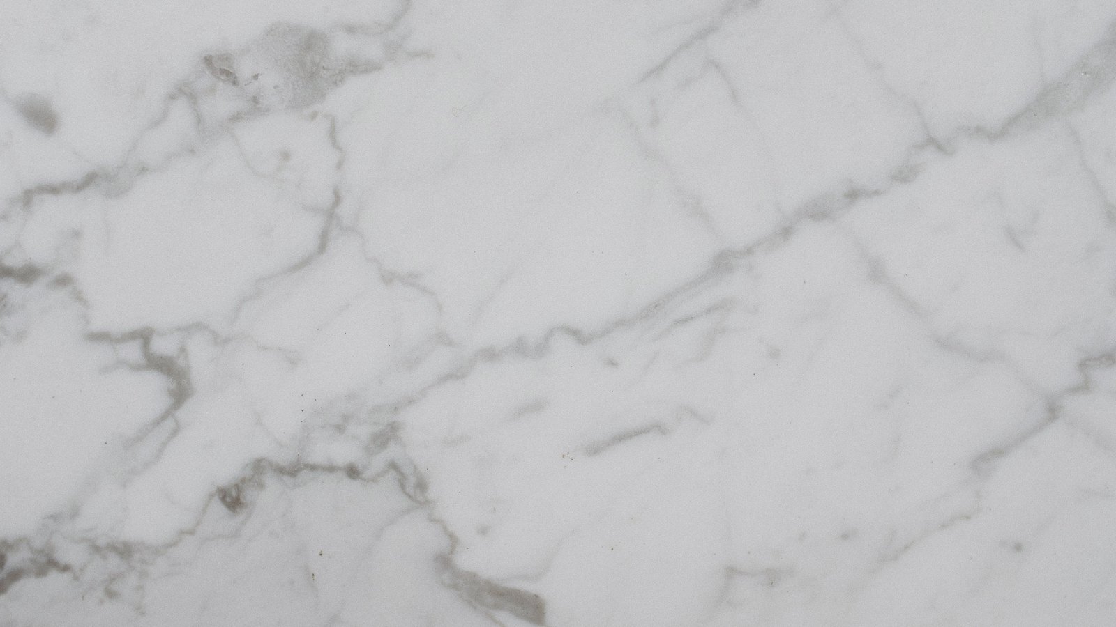 A close macro of polished white marble, with fine grey veins branching diagonally from the lower left towards the upper right.