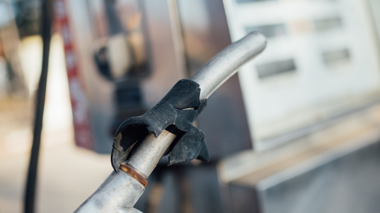 A close-up of a metal fuel nozzle resting beside a blurred fuel pump.