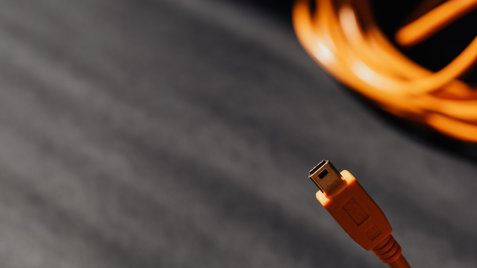 An orange cable coiled on grey fabric, its metal connector head standing upright in sharp focus in the foreground.
