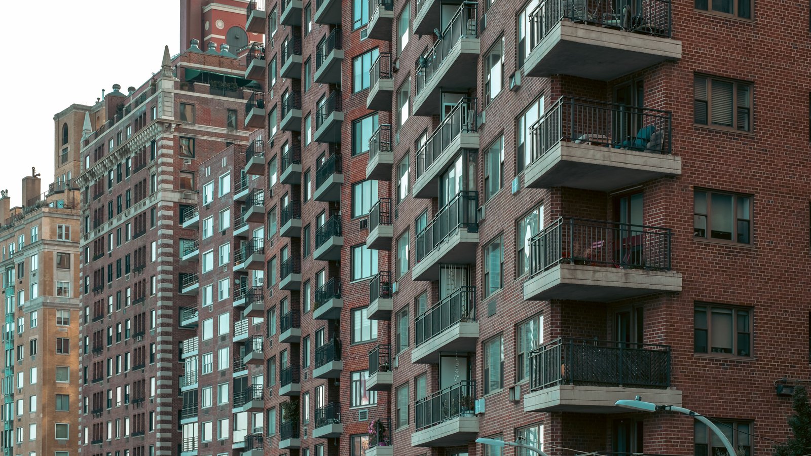 Brick apartment towers in New York City packed side by side, their facades stacked with concrete balconies and metal railings, seen from street level with no signage in frame.