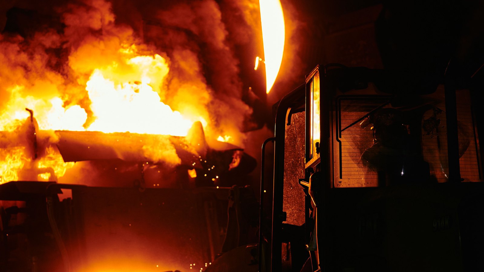 Flames and molten metal glow inside an industrial foundry at night.