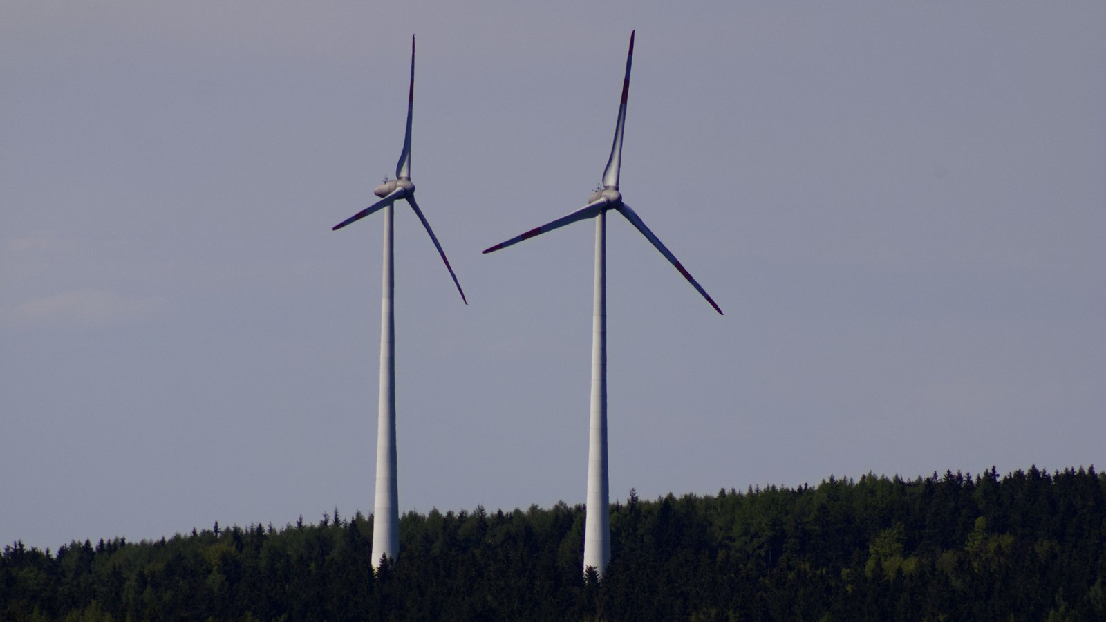 Two wind turbines above a wooded hillside in the German countryside