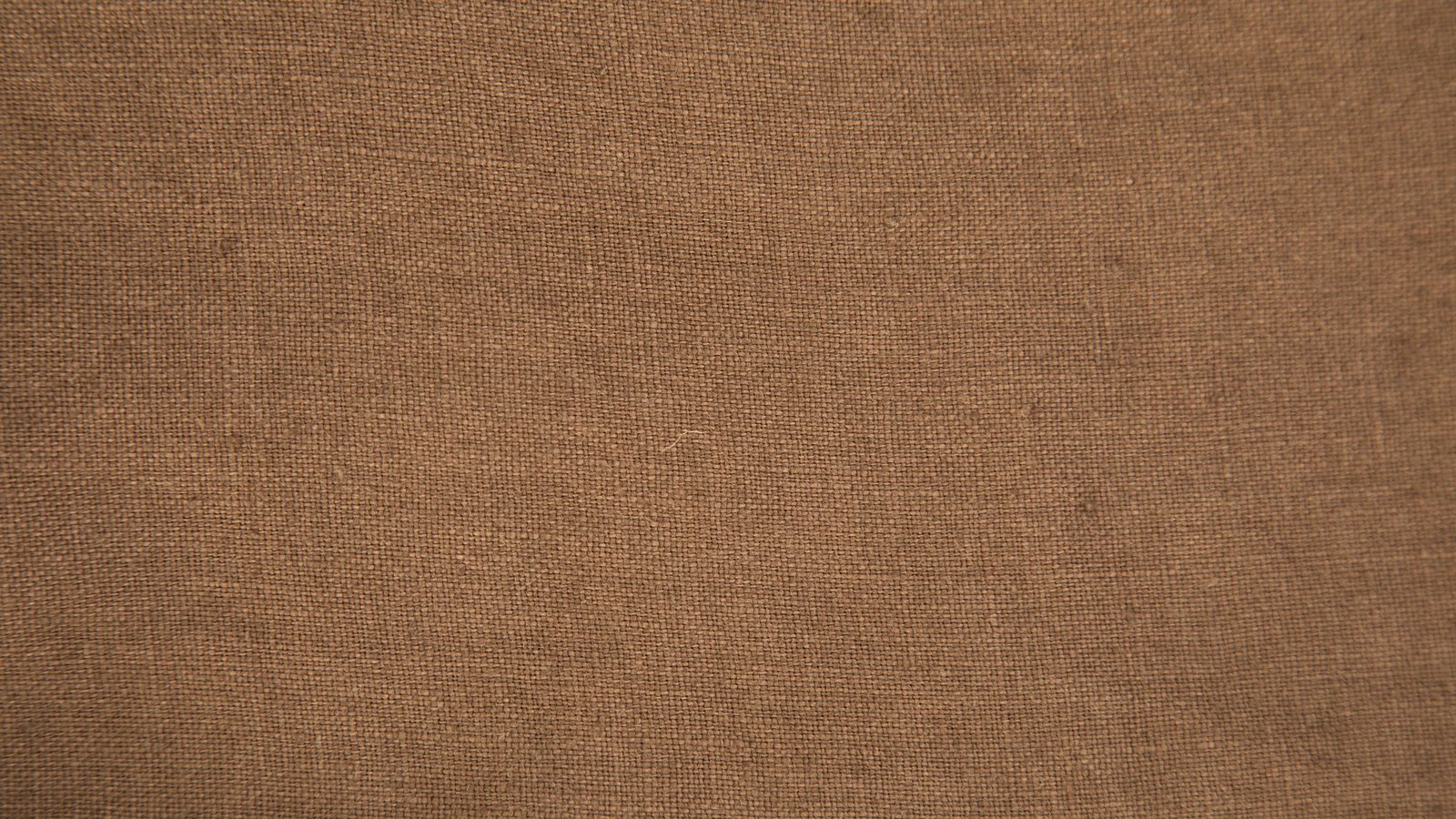 A close photograph of plain woven brown linen filling the whole frame, the weave visible as fine even crossings of warp and weft with occasional thicker slubs running through it, evenly lit, with no text, objects or horizon in view.