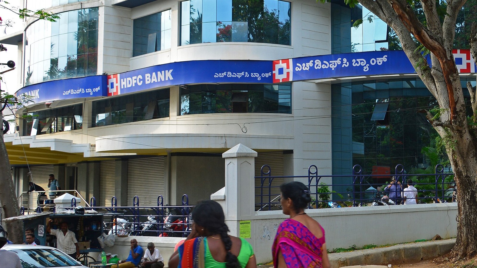 HDFC Bank branding on the curved facade of its Temple Road branch in Mysore, partly shaded by trees.