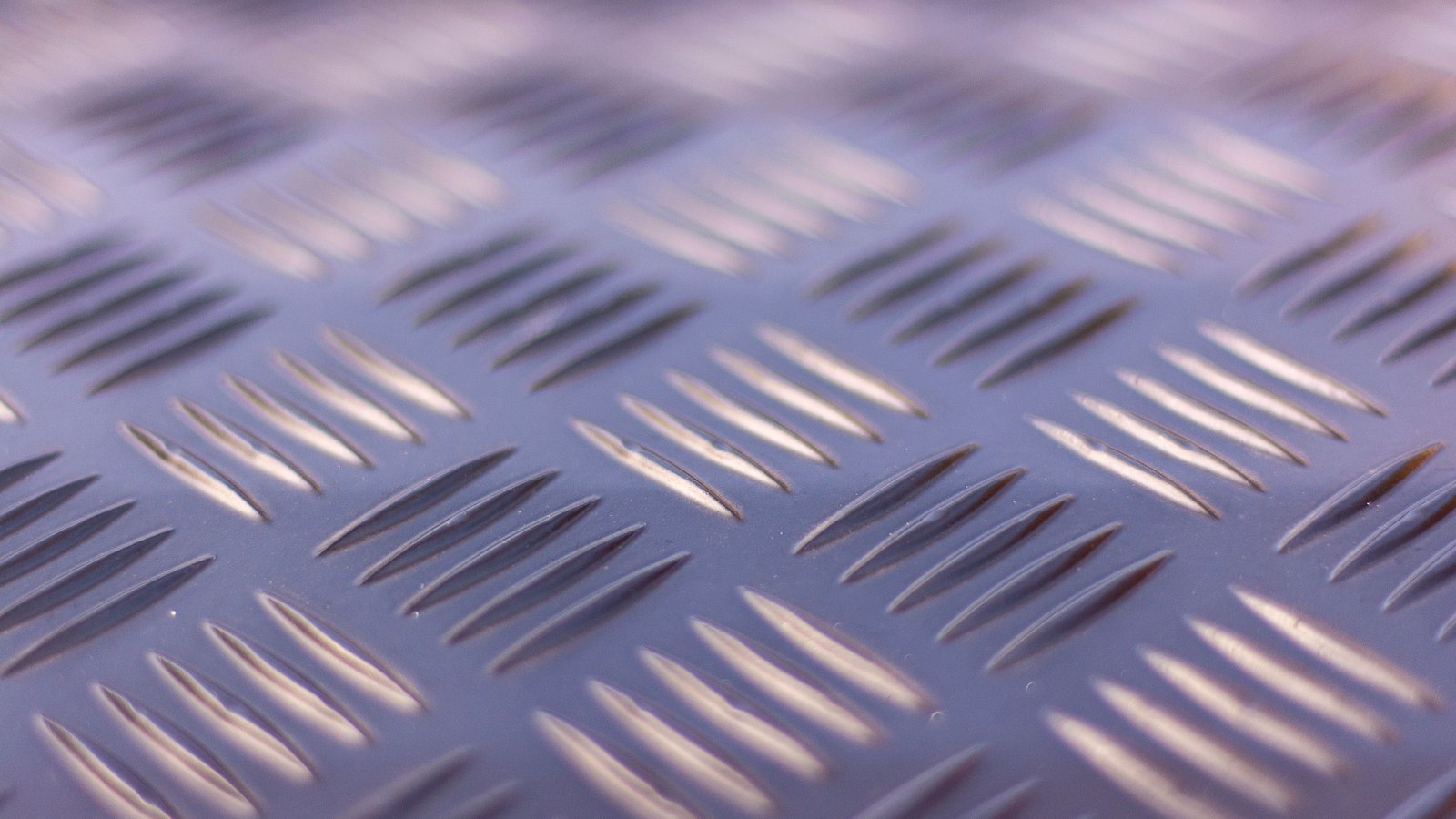 Close view of raised chequer plate steel, the diamond anti-slip pattern running in diagonal rows and catching a low light.