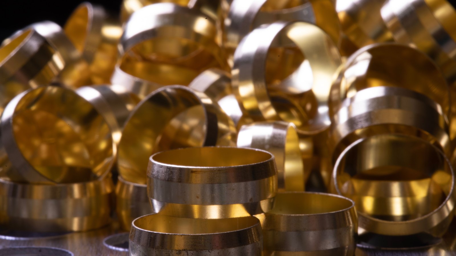 A close view of a heap of machined brass ring fittings, their turned edges catching warm light.