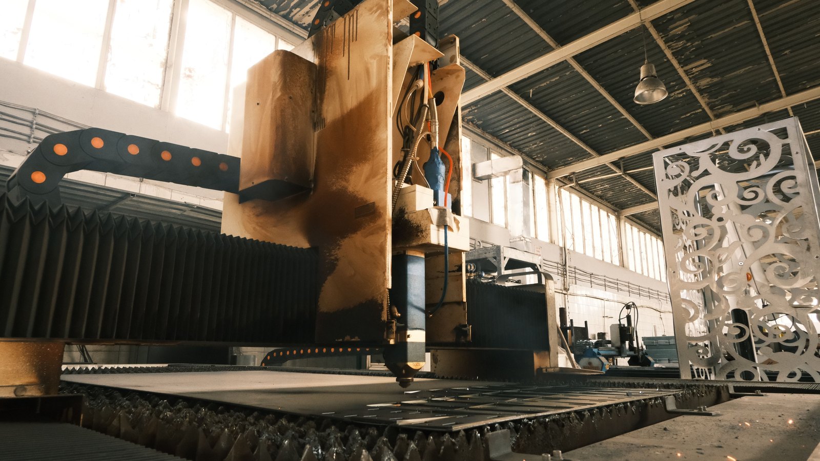 A laser cutter works across a sheet of metal inside an industrial plant.