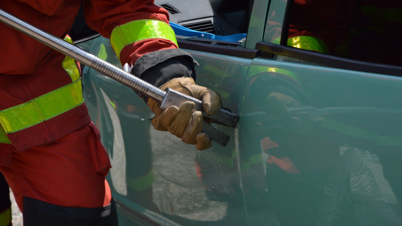 A firefighter in turnout gear uses a pry bar on a damaged car door during a rescue exercise, not a photograph of this event.