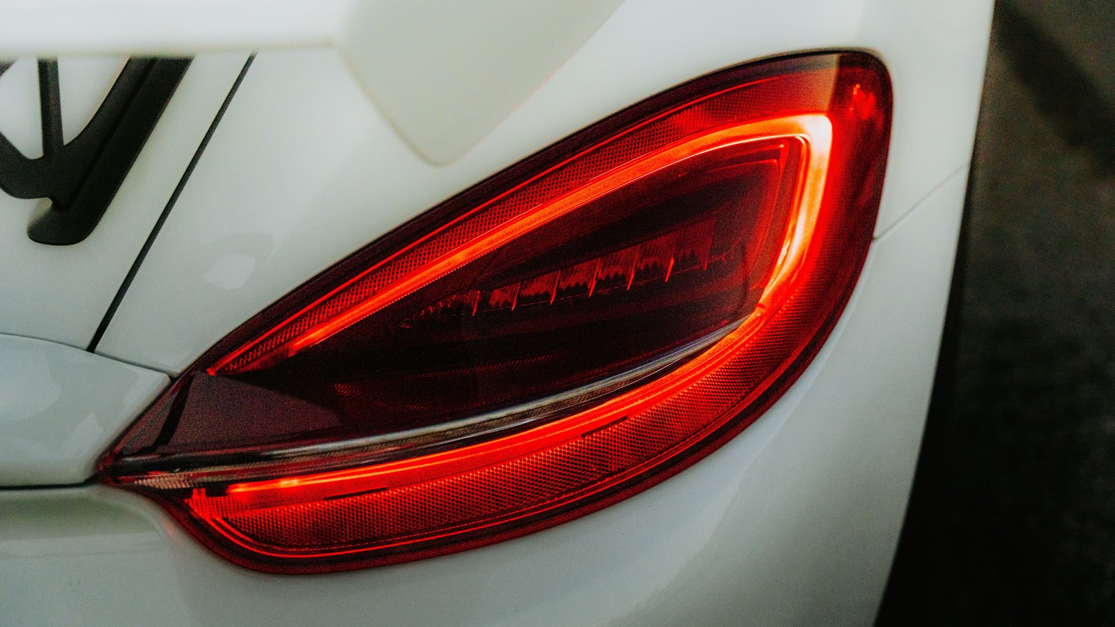 A tight crop of a red tail light glowing on the rear of a white car, the lens lit and the surrounding bodywork clean and unmarked. No number plate, manufacturer badge, model name or legible text of any kind is in the frame, no person appears, and nothing identifies the vehicle or the place. A generic illustration of a braking vehicle, not a photograph of either vehicle in this crash and not a photograph of this event.