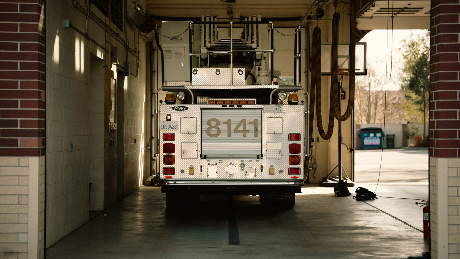 The rear of a fire department ladder truck parked in a station bay, its diamond plate tailboard and a unit number visible under the roll up door. No department name, plate, person or location is identifiable. A generic illustration of fire apparatus, not a photograph of this vehicle fire or of Interstate 75.