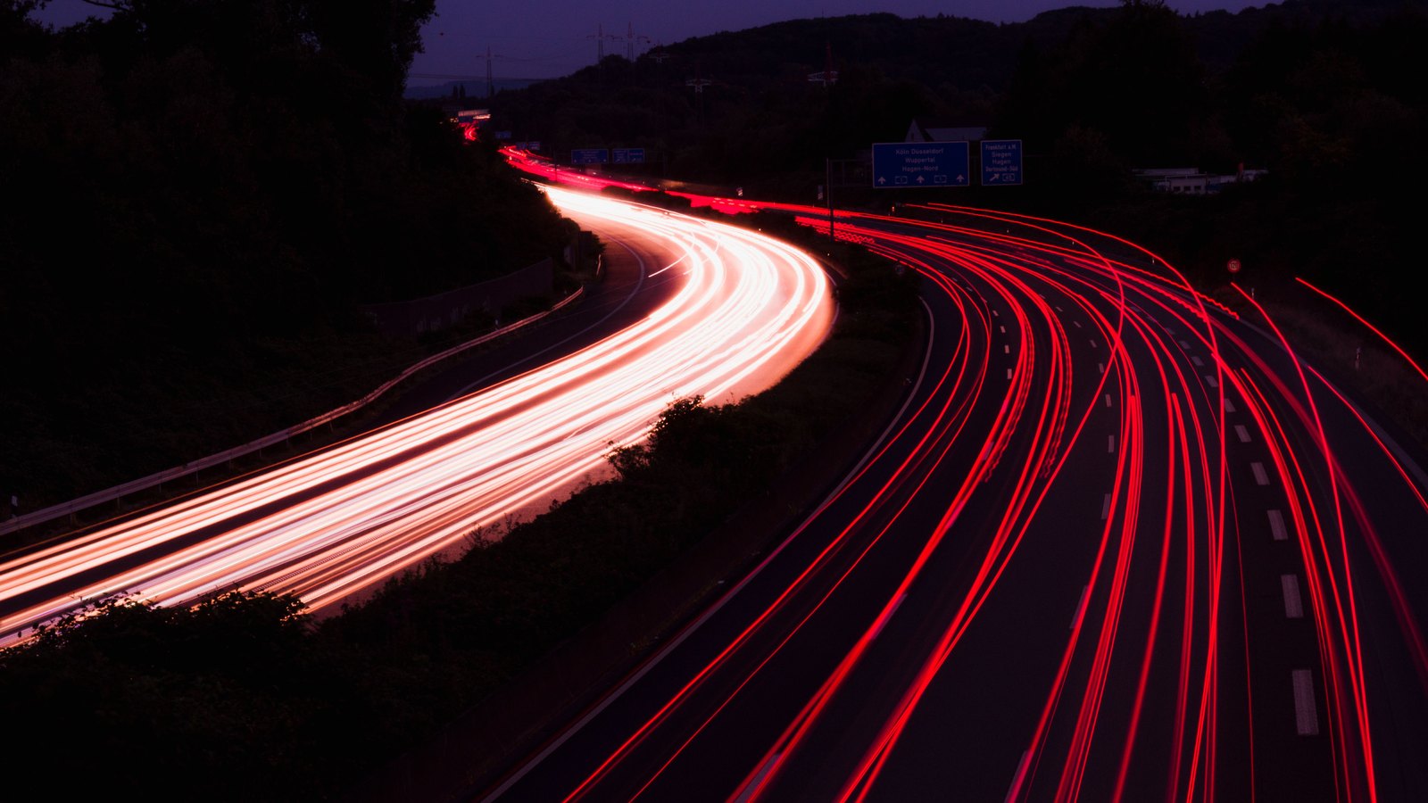 Long-exposure red tail-light trails along a highway at night.