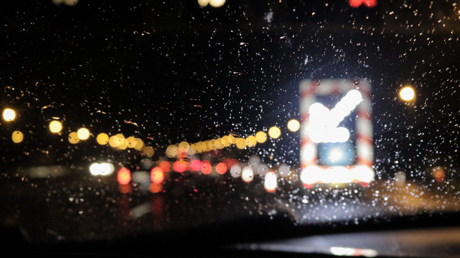 Traffic seen through a rain covered windshield at night, with vehicle lights out of focus and no readable text, not a photograph of this event.