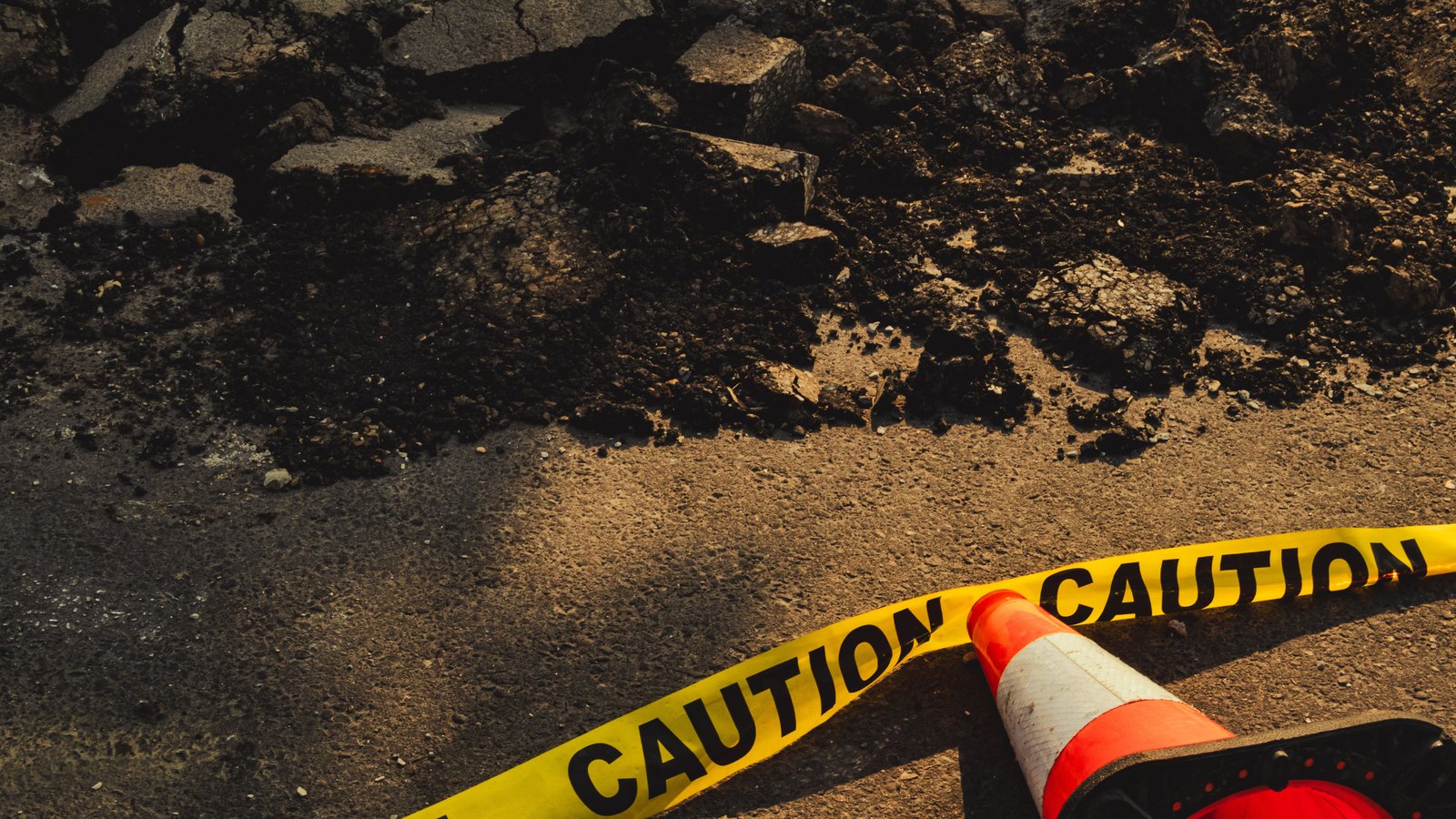 Yellow caution tape runs across broken pavement beside an orange traffic cone, a stock photograph and not the crash or Alligator Alley.