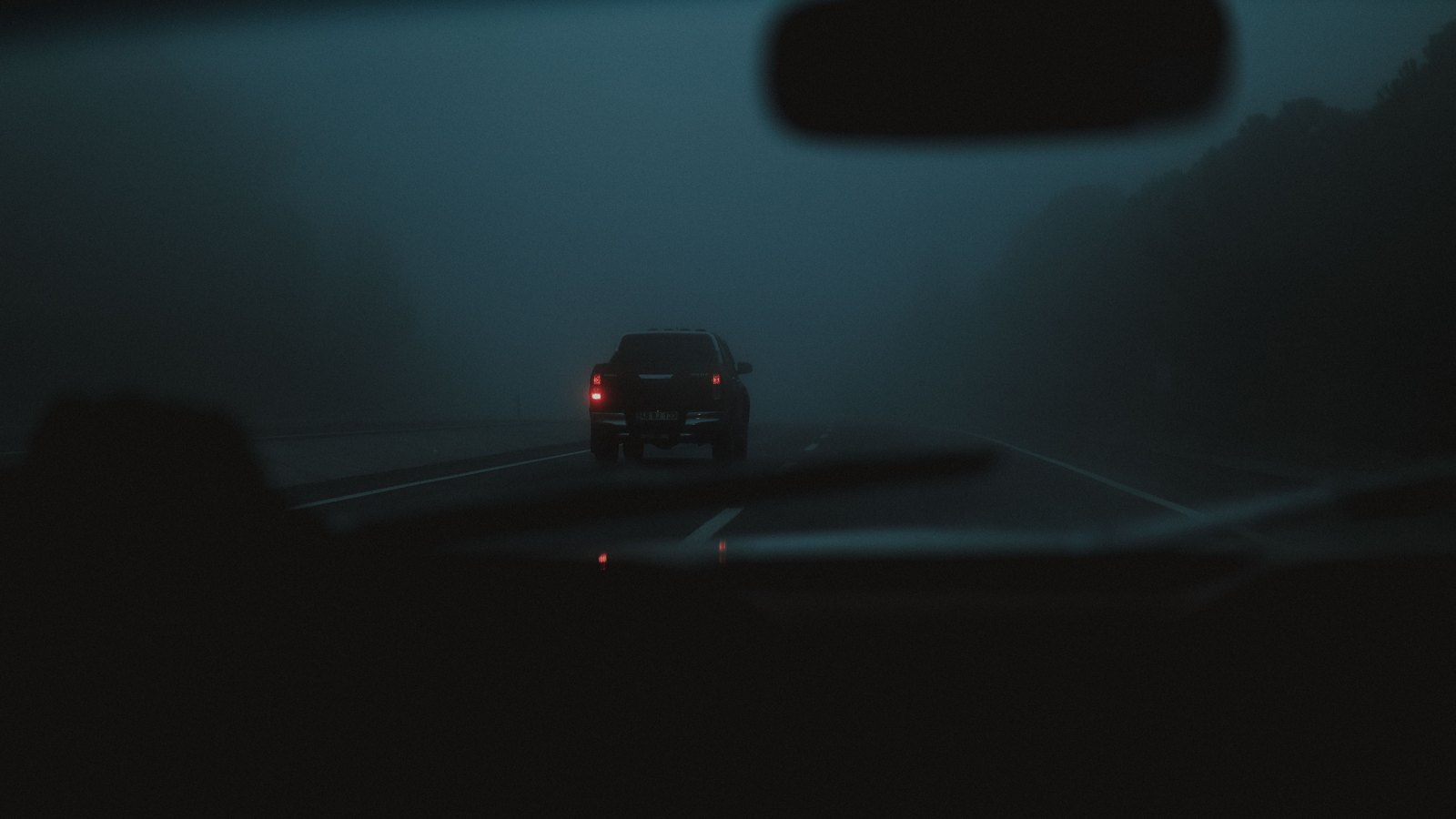 A vehicle ahead seen through a windshield in dense fog at night, not a photograph of this event.