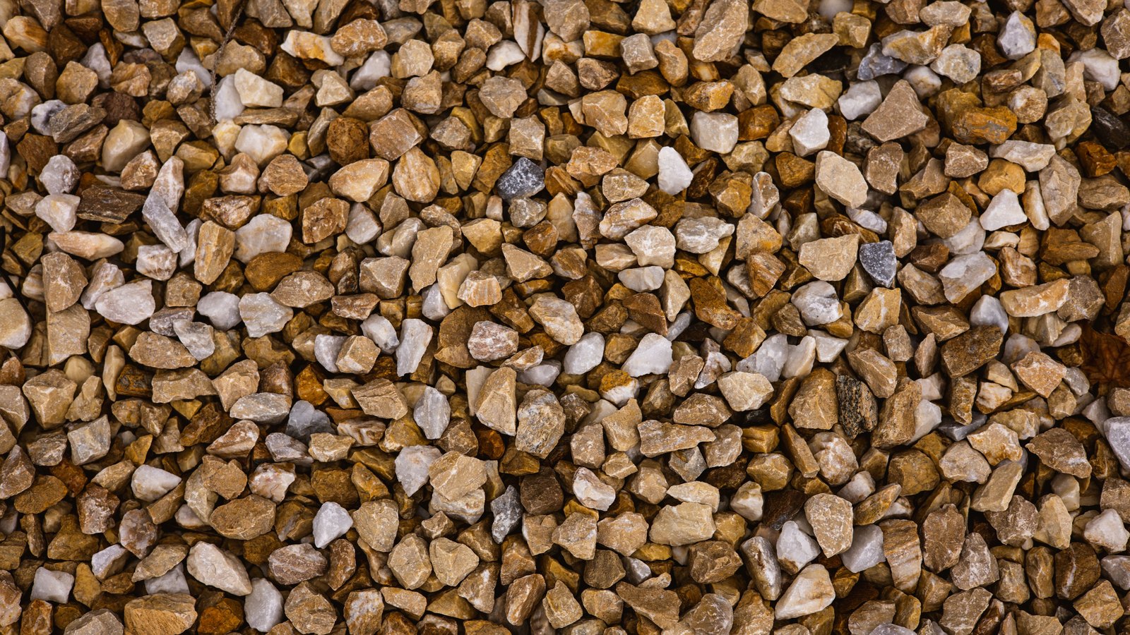 A close overhead crop of small crushed stone chippings filling the frame, mostly tan, gold and brown with scattered off white and grey pieces. It is used as an illustration and is not a photograph of this crash or of this stretch of Interstate 75.