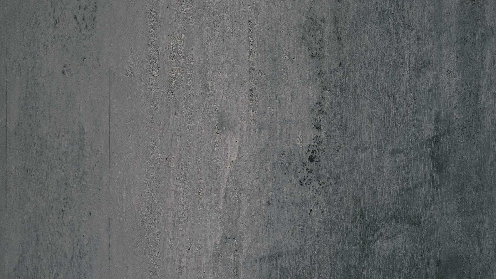 A plain grey concrete wall filling the frame, pale and faintly streaked down the left side and darkening towards the right.