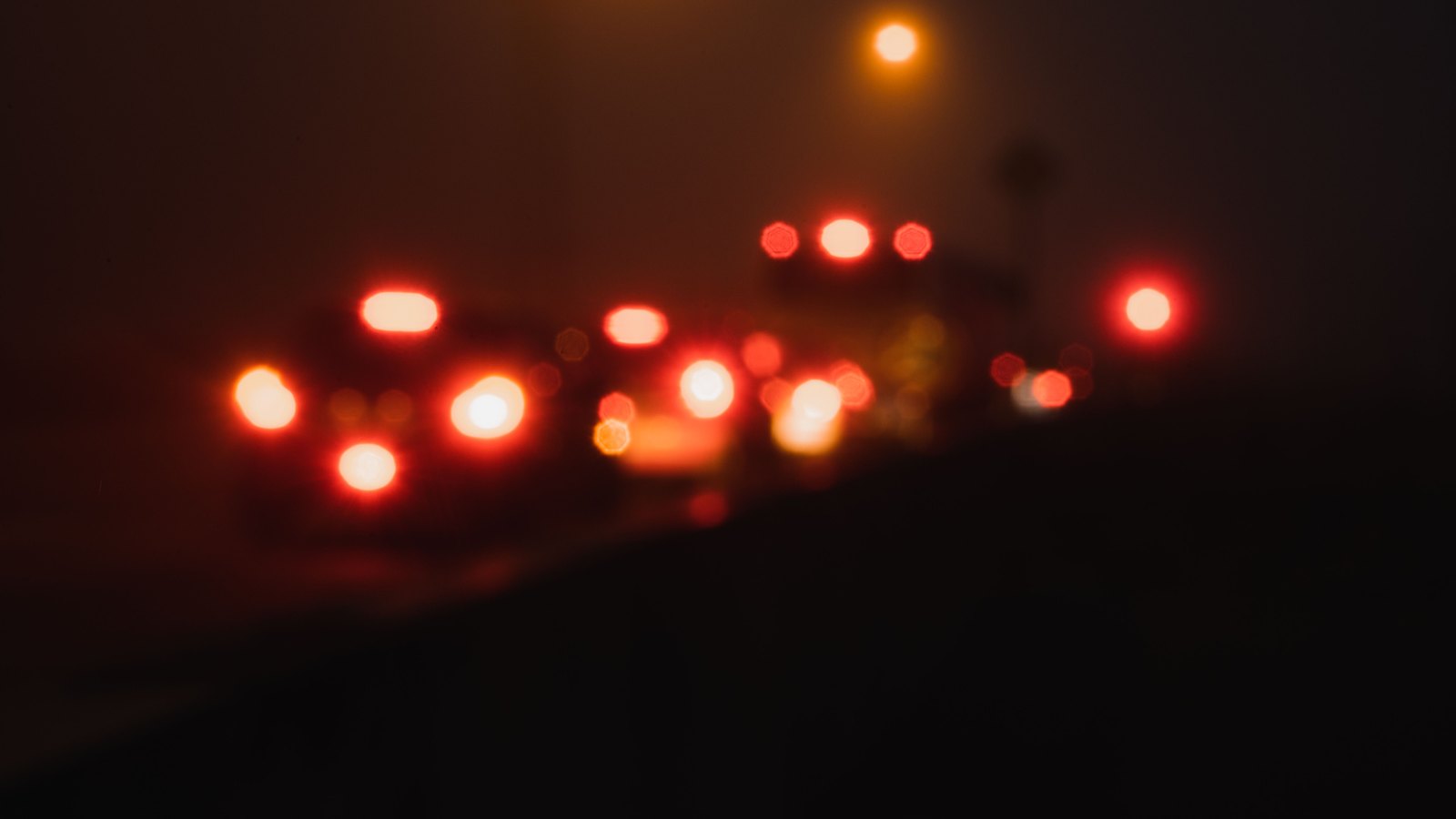 Defocused red and amber vehicle lights on a dark roadway, with no person, readable plate, sign, agency marking or identifiable place visible, not a photograph of this event.