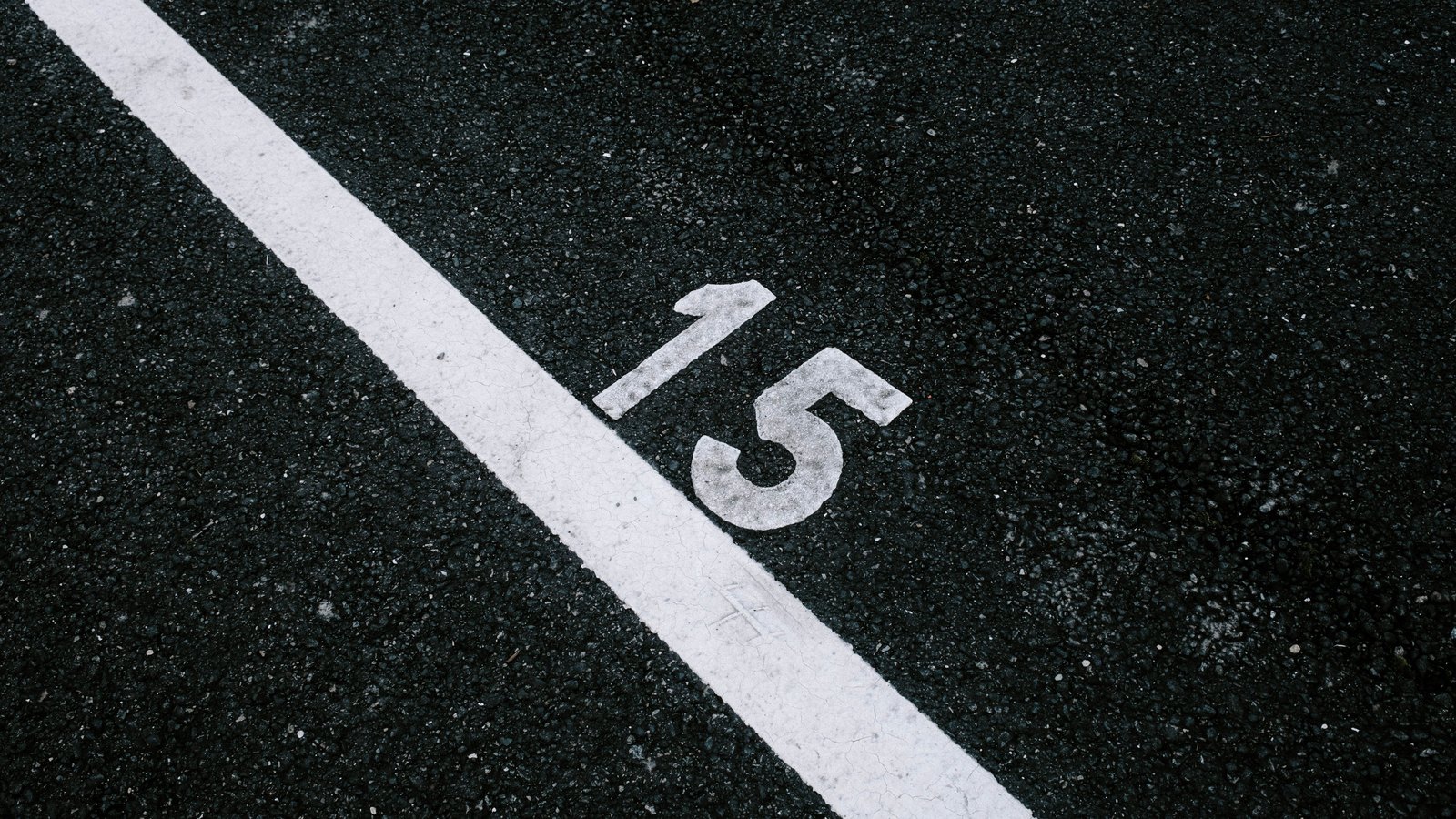 A white painted line and the number 15 stenciled on dark asphalt pavement.