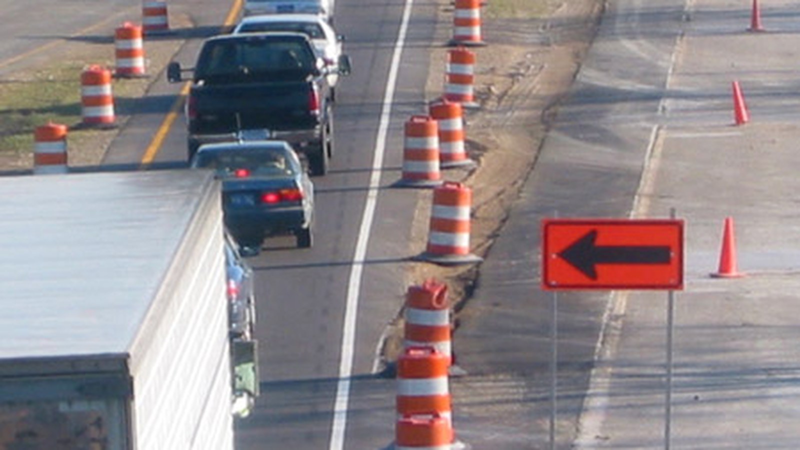 Traffic moves beside orange work-zone barrels and a lane-direction arrow, not a photograph of this event.