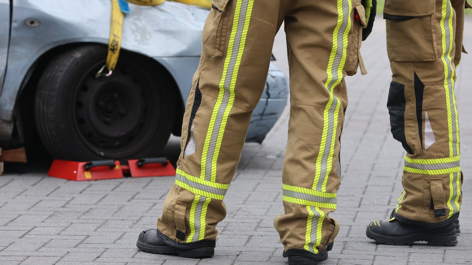 Firefighters in reflective gear stand beside a damaged car, a stock image not a photograph of this event.