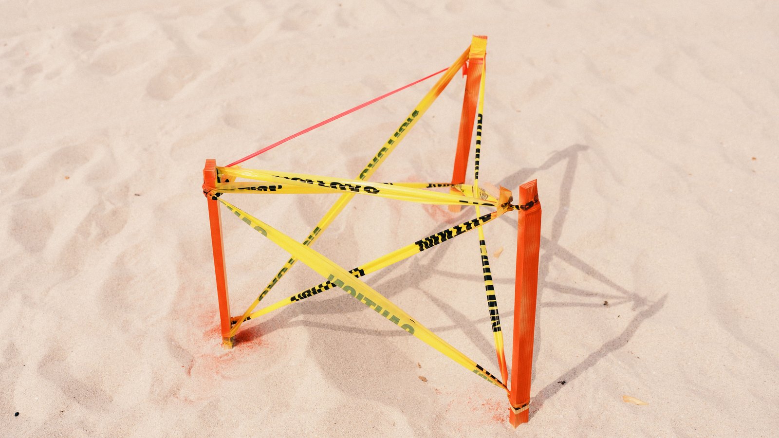 Yellow caution tape wrapped around orange stakes in sandy ground; not a photograph of this event.