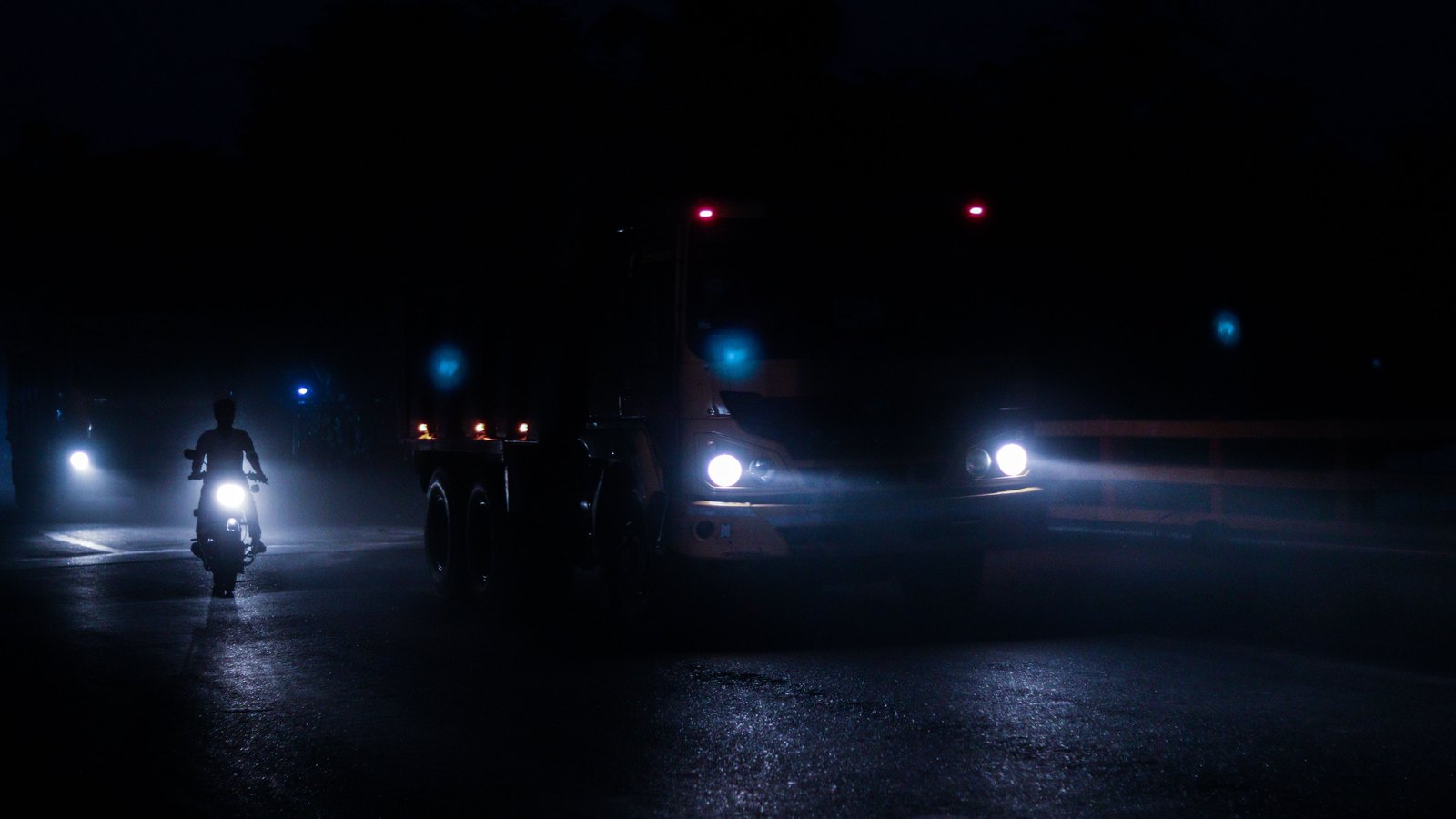 Headlights from a truck, a motorcycle and other vehicles cut through mist on a dark roadway. No person is identifiable. A generic stock image, not a photograph of this event.