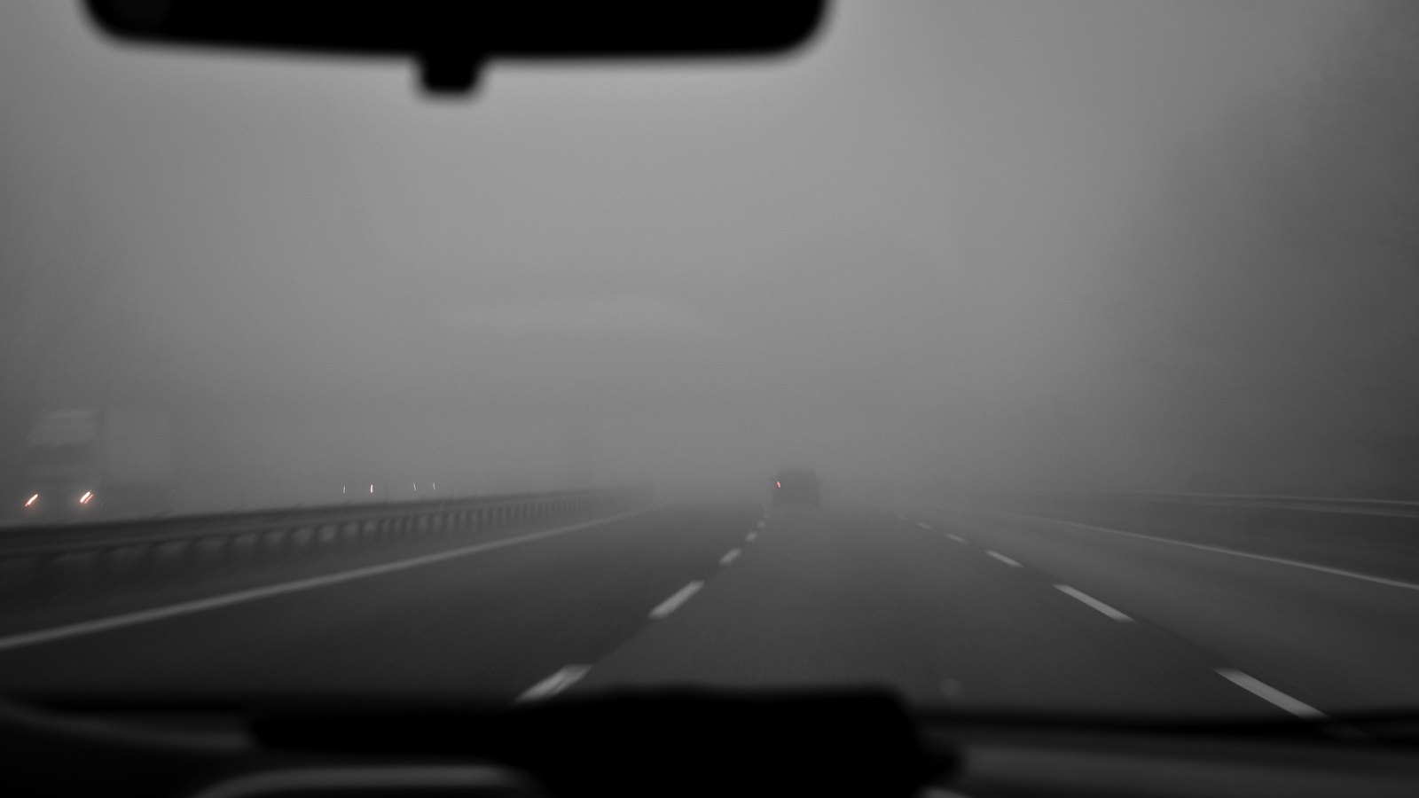 A driver's view through a windshield of vehicles disappearing into dense fog on a multilane highway, not a photograph of this event.