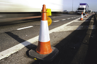 An orange traffic cone with a warning light stands beside a highway lane, not a photograph of this event.