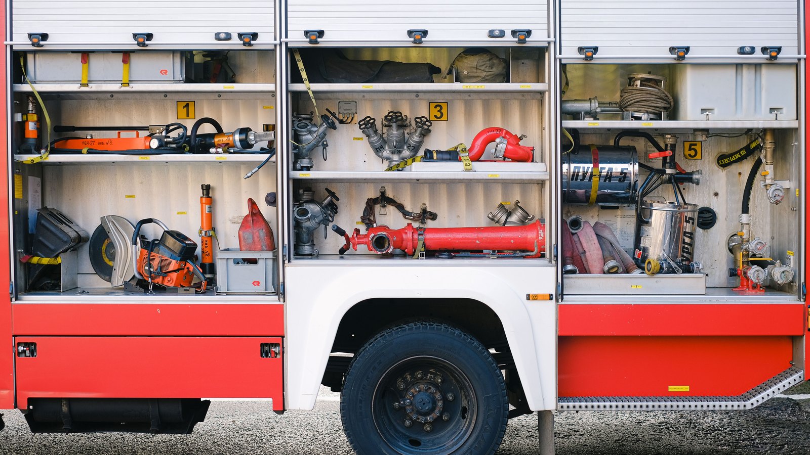 Open compartments on a red fire engine display hoses and rescue tools, not a photograph of this event.