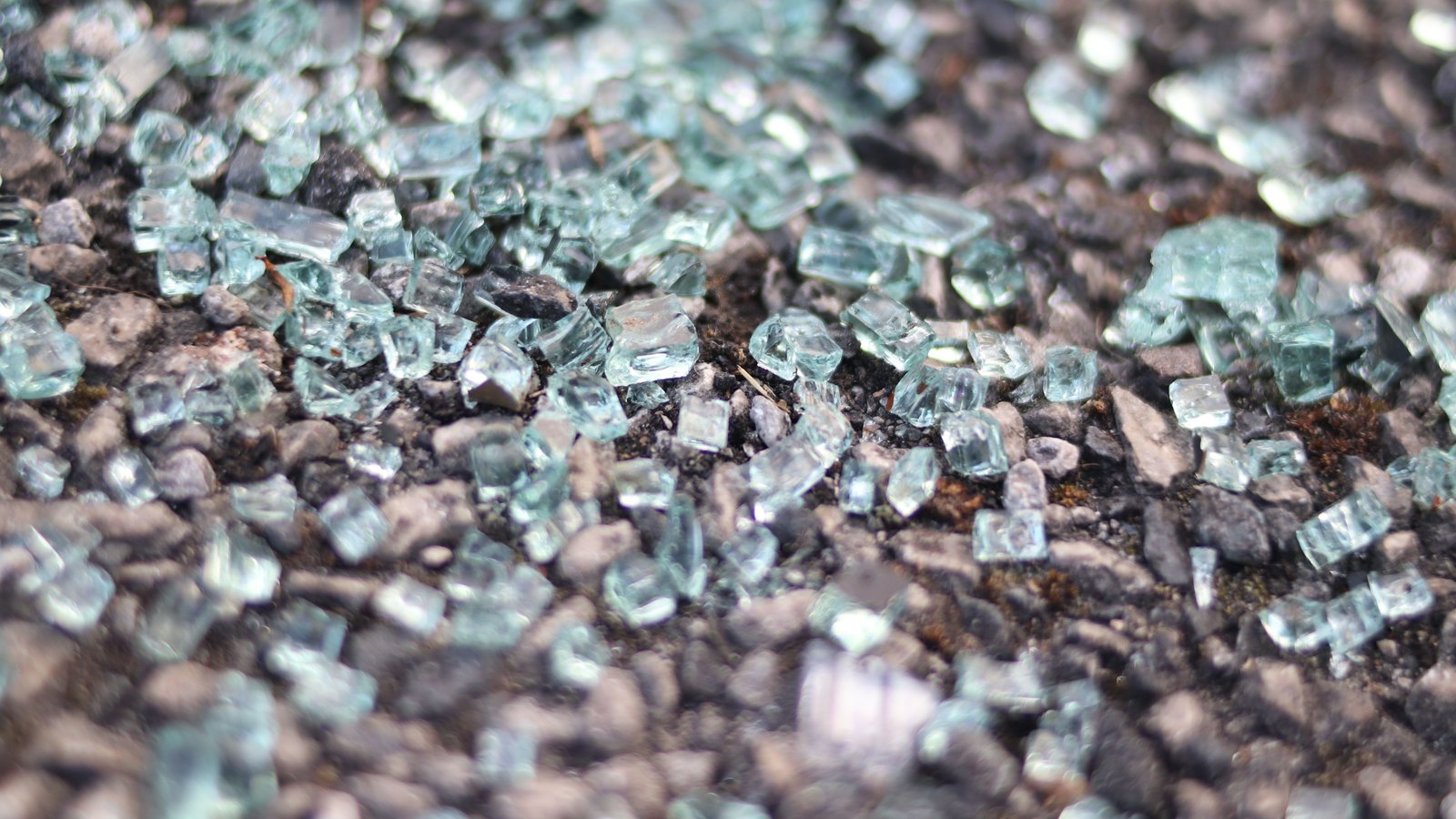Shattered glass scattered across a rough roadway surface.