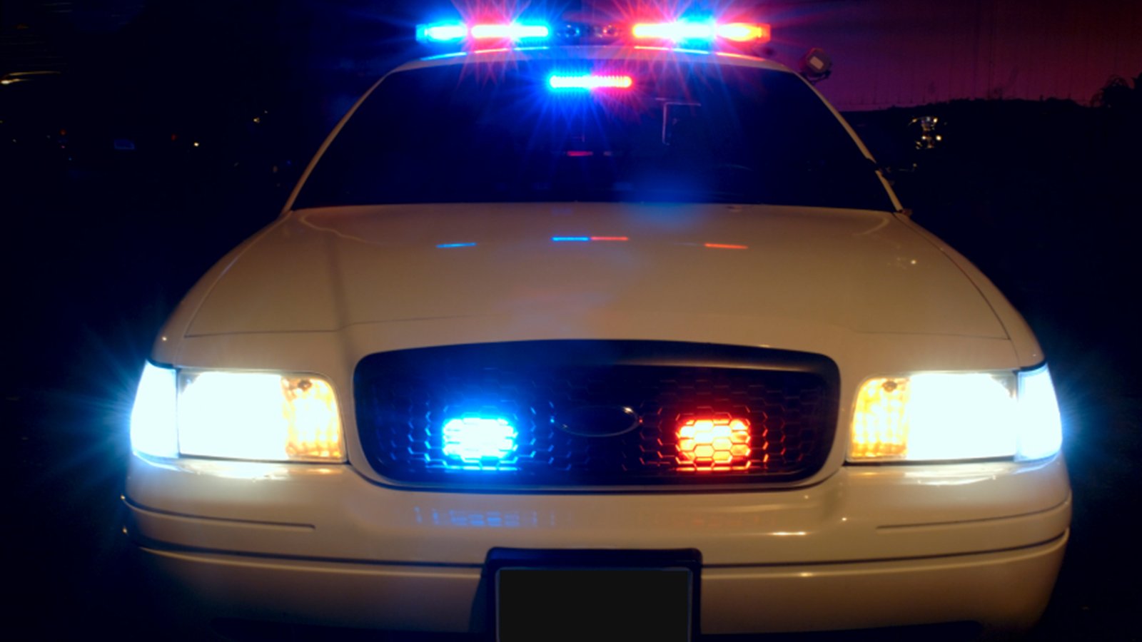 Red and blue emergency lights flash on a generic unmarked police car at night, not a photograph of this crash.