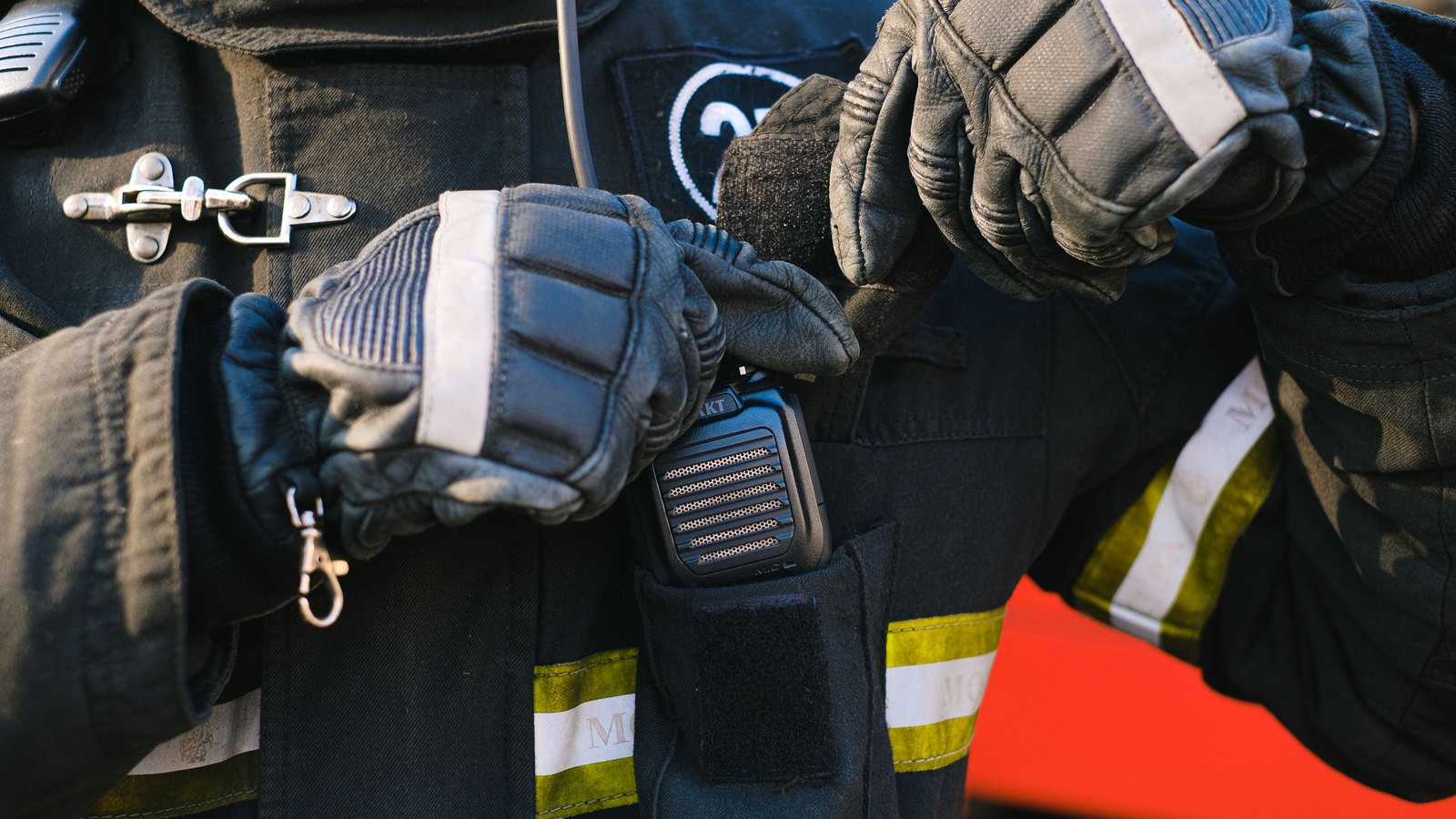 A close view of a firefighter in turnout gear using a radio, with the face and agency markings outside the frame; not a photograph of this event.