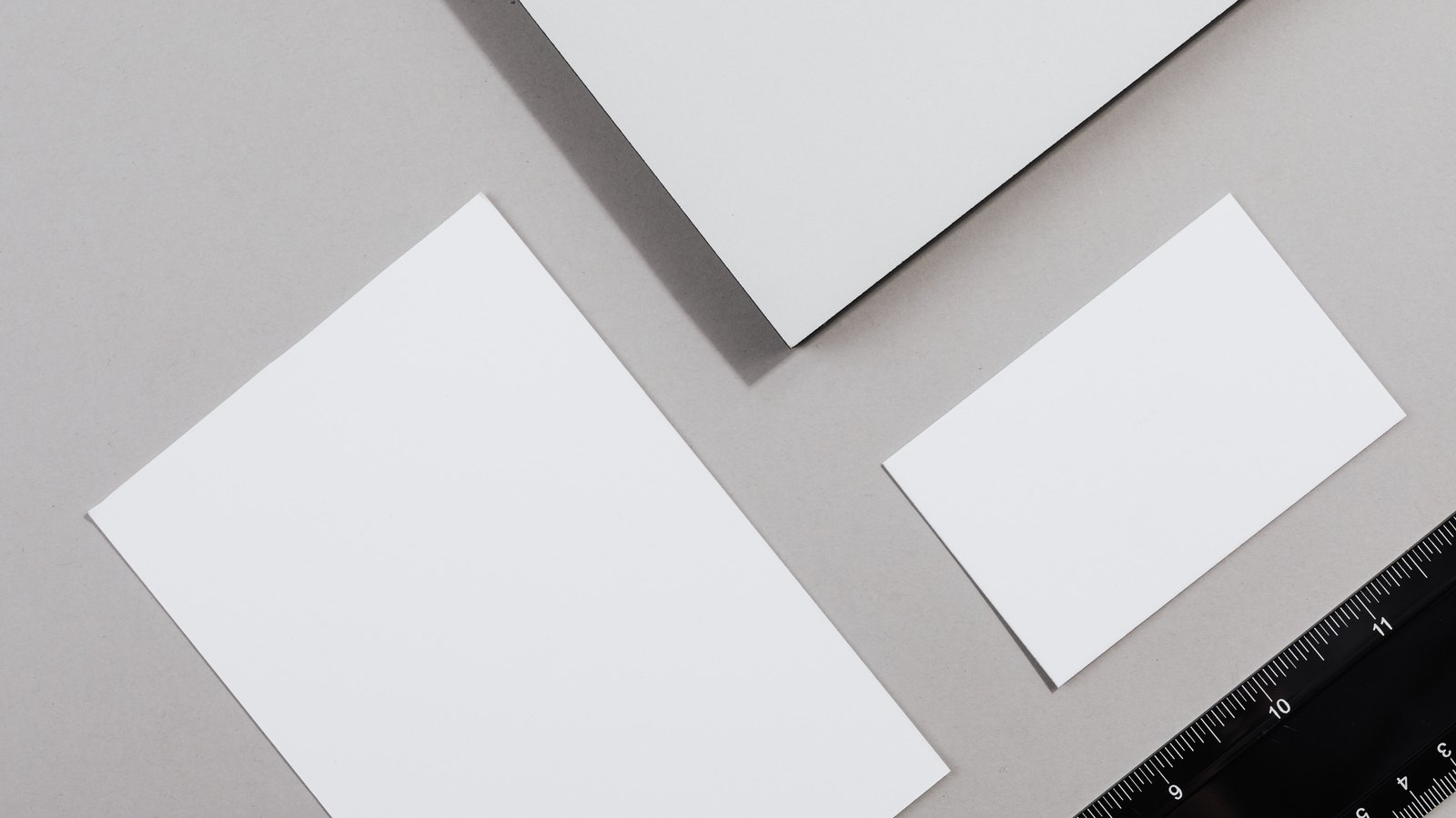 An overhead photograph of three blank white sheets of paper of different sizes arranged on a plain grey surface, with the corner of a black ruler entering the frame at the lower right. Nothing is written or printed on any of the sheets. No people, faces, places, logos or readable text appear. A generic illustration of paperwork, not a photograph of any court record in this case.