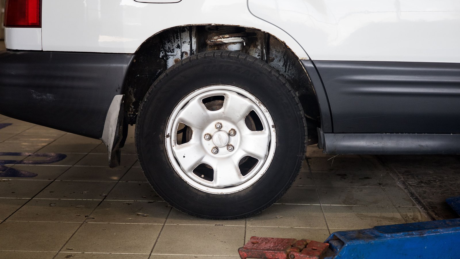 A vehicle wheel sits above a service jack in a close roadside-assistance view, not a photograph of this event.