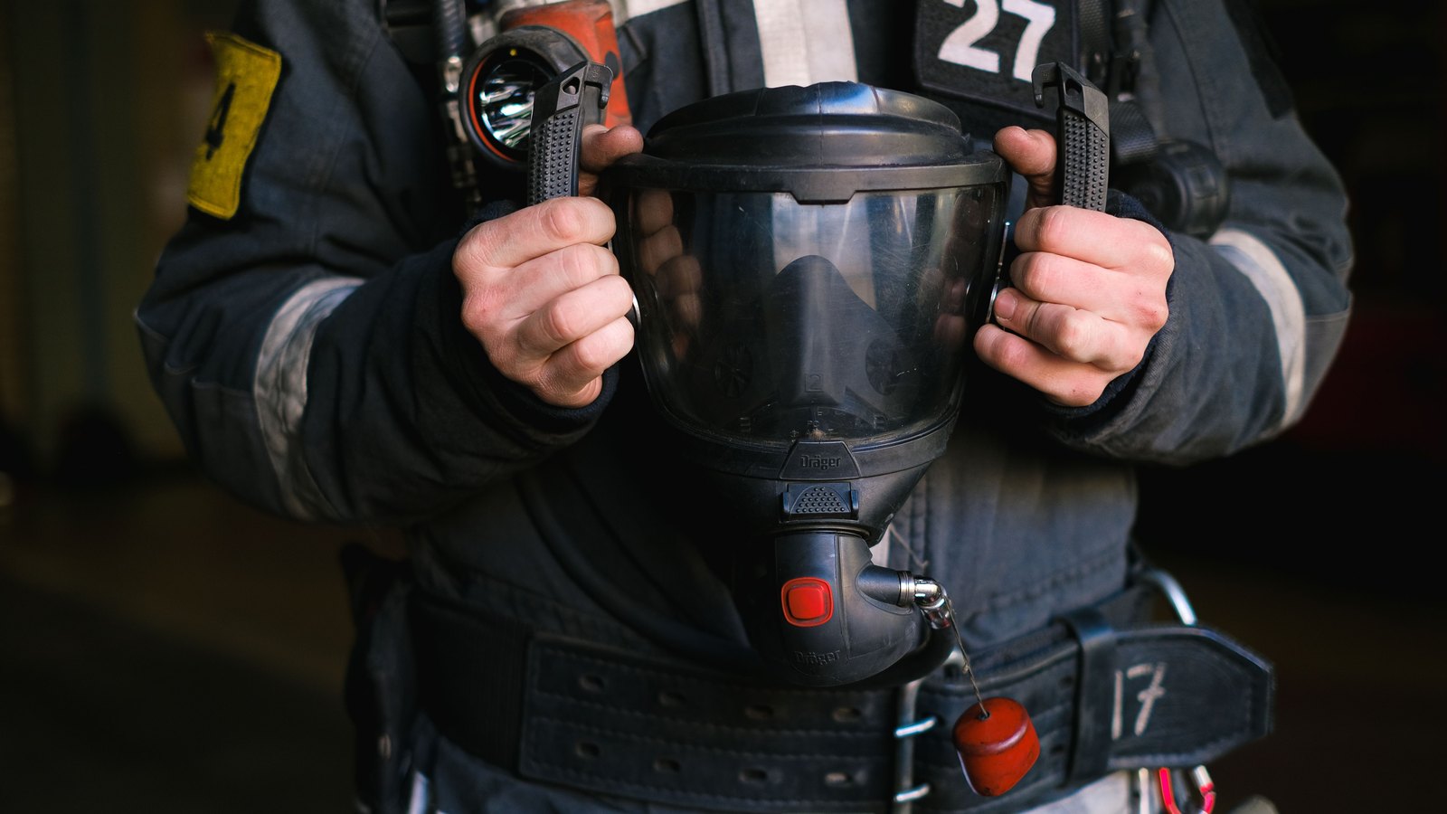 A firefighter holds a protective breathing mask against turnout gear, not a photograph of this event.
