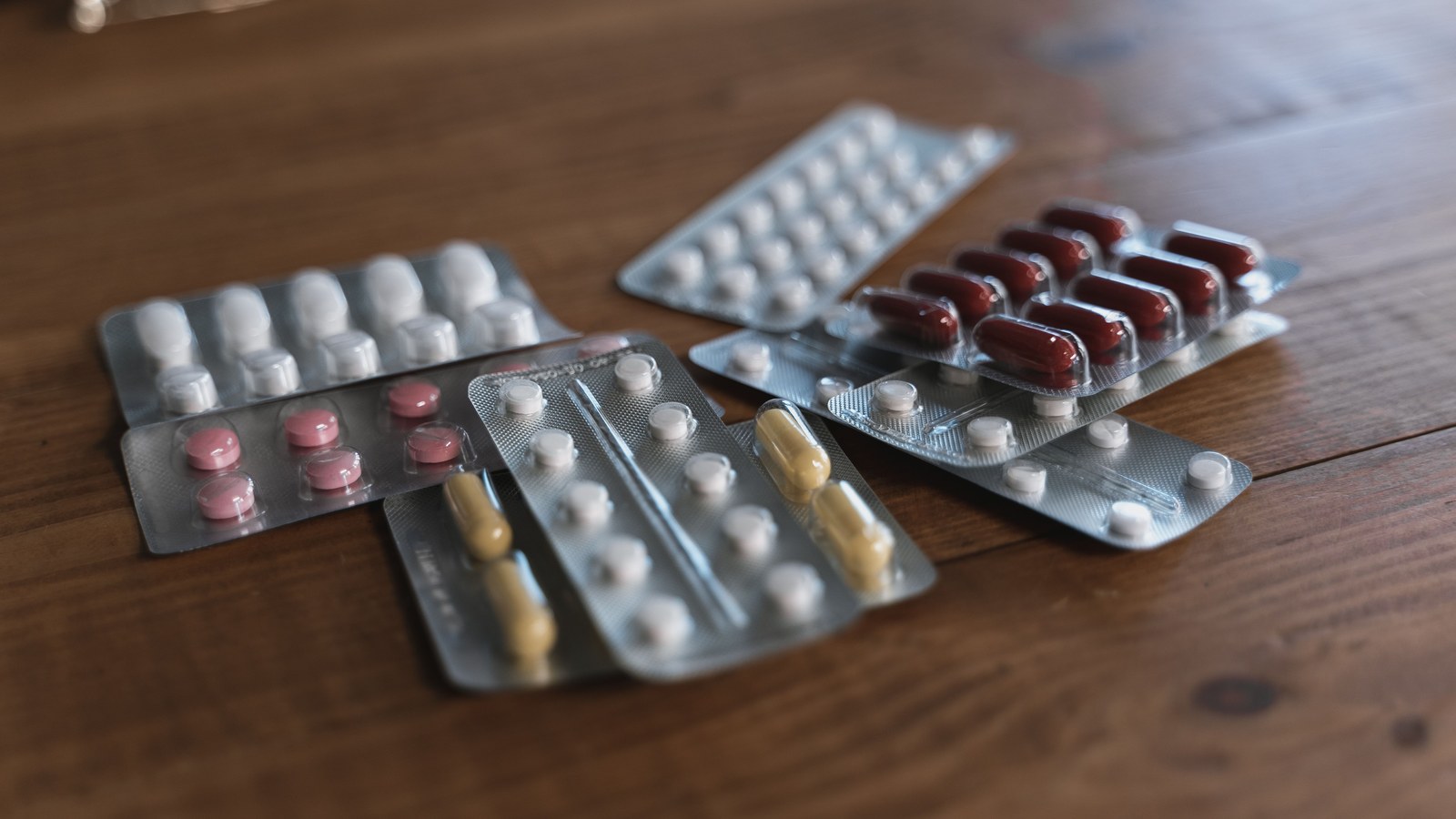 Blister packs of tablets and capsules arranged on a wooden surface.